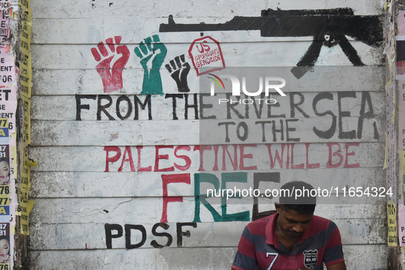 A person sits next to a mural about the Palestine and Israel war in Kolkata, India, on October 10, 2024. 