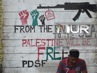 A person sits next to a mural about the Palestine and Israel war in Kolkata, India, on October 10, 2024. (