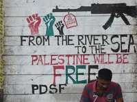 A person sits next to a mural about the Palestine and Israel war in Kolkata, India, on October 10, 2024. (