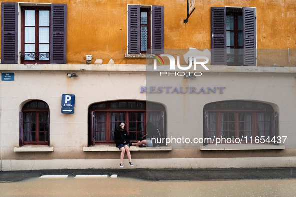 Two young people sit next to a flooded street in Coulommiers, Seine-et-Marne department, east of Paris, on October 10, 2024, as the heavy ra...