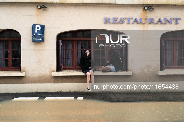 Two young people sit next to a flooded street in Coulommiers, Seine-et-Marne department, east of Paris, on October 10, 2024, as the heavy ra...