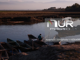 A boy from a fishing community removes water from a boat at Wular Lake in Sopore, Jammu and Kashmir, India, on October 11, 2024. (