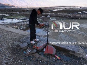 A boy tries to close a faulty tap installed on a roadside at Wular Lake in Sopore, Jammu and Kashmir, India, on October 11, 2024. (