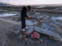 A boy tries to close a faulty tap installed on a roadside at Wular Lake in Sopore, Jammu and Kashmir, India, on October 11, 2024. (