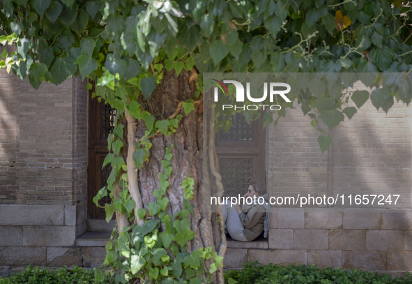 An Iranian woman sits in front of a room near the tomb of the 14th-century Iranian poet Hafez in Shiraz, Iran, on October 8, 2024.  