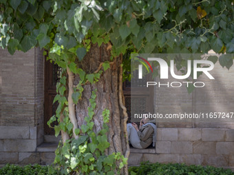 An Iranian woman sits in front of a room near the tomb of the 14th-century Iranian poet Hafez in Shiraz, Iran, on October 8, 2024.  (