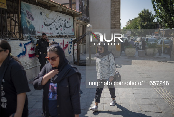 An Iranian policeman looks at young women walking along a sidewalk out of a holy shrine in Shiraz, Iran, on October 8, 2024.  