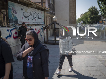 An Iranian policeman looks at young women walking along a sidewalk out of a holy shrine in Shiraz, Iran, on October 8, 2024.  (