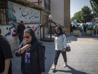 An Iranian policeman looks at young women walking along a sidewalk out of a holy shrine in Shiraz, Iran, on October 8, 2024.  (