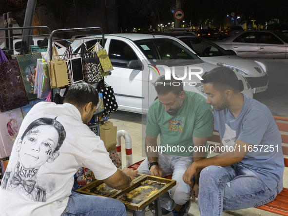 Young Iranian men play backgammon while sitting on a sidewalk outside a shopping center in Shiraz, Iran, on October 8, 2024, at night.  