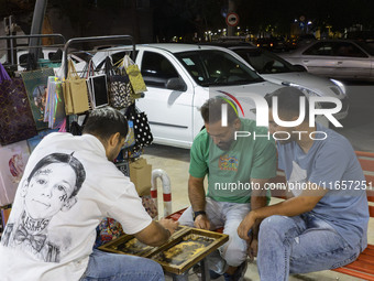 Young Iranian men play backgammon while sitting on a sidewalk outside a shopping center in Shiraz, Iran, on October 8, 2024, at night.  (