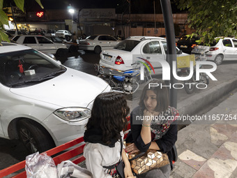 Two young Iranian women who are not wearing mandatory headscarves sit together on a sidewalk outside a shopping center in Shiraz, Iran, on O...