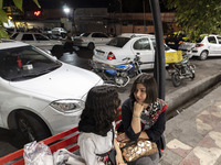 Two young Iranian women who are not wearing mandatory headscarves sit together on a sidewalk outside a shopping center in Shiraz, Iran, on O...