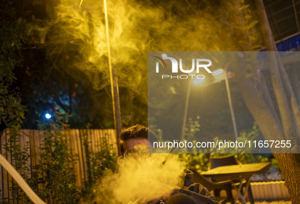 A young Iranian man puffs on a hookah while sitting at a garden-cafe in Shiraz, Iran, on October 7, 2024.  