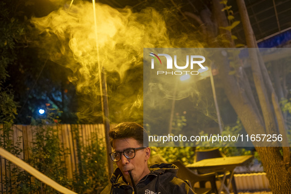 A young Iranian man puffs on a hookah while sitting at a garden-cafe in Shiraz, Iran, on October 7, 2024.  