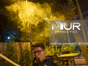 A young Iranian man puffs on a hookah while sitting at a garden-cafe in Shiraz, Iran, on October 7, 2024.  (