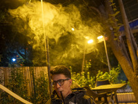 A young Iranian man puffs on a hookah while sitting at a garden-cafe in Shiraz, Iran, on October 7, 2024.  (