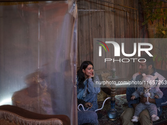 A young woman and a man carrying his child sit at a garden cafe in Shiraz, Iran, on October 7, 2024.  (