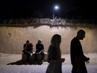 Iranian youths walk past young men sitting on a path in Shiraz, Iran, on October 7, 2024, at night.  (