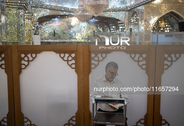 An Iranian man reads a copy of the Muslim holy book, the Koran, while sitting next to a tomb in a holy shrine in Shiraz, Iran, on October 8,...