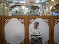 An Iranian man reads a copy of the Muslim holy book, the Koran, while sitting next to a tomb in a holy shrine in Shiraz, Iran, on October 8,...