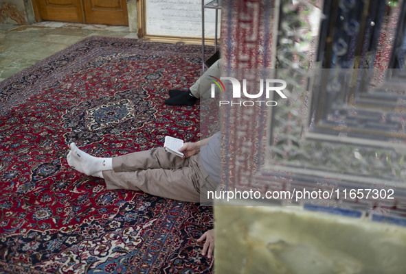 An Iranian man reads a prayer book while sitting next to a tomb in a holy shrine in Shiraz, Iran, on October 8, 2024. Western countries expr...