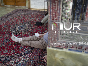 An Iranian man reads a prayer book while sitting next to a tomb in a holy shrine in Shiraz, Iran, on October 8, 2024. Western countries expr...