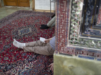 An Iranian man reads a prayer book while sitting next to a tomb in a holy shrine in Shiraz, Iran, on October 8, 2024. Western countries expr...