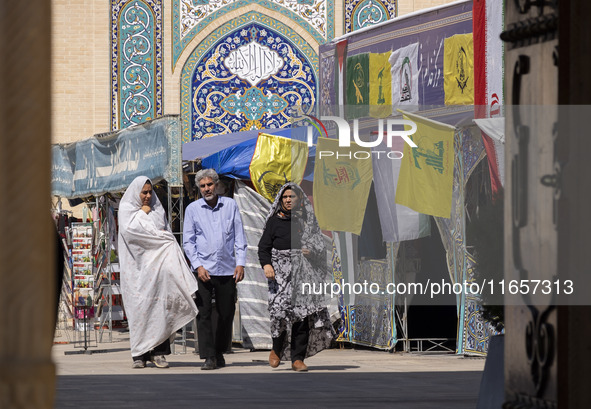 Two veiled Iranian women and a man walk past Lebanon's Hezbollah flags in a holy shrine in Shiraz, Iran, on October 8, 2024. While Western c...