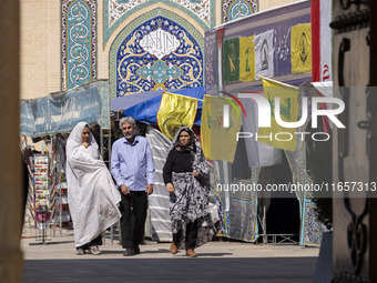 Two veiled Iranian women and a man walk past Lebanon's Hezbollah flags in a holy shrine in Shiraz, Iran, on October 8, 2024. While Western c...