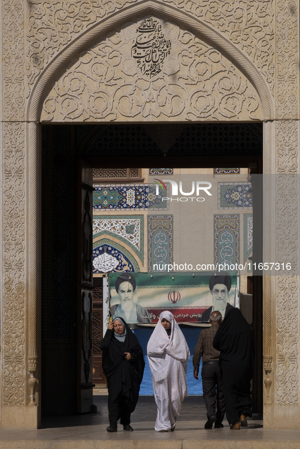 Two veiled Iranian women walk under a banner featuring portraits of Iran's Supreme Leader, Ayatollah Ali Khamenei, and the late leader, Ayat...