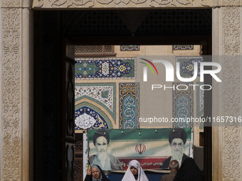 Two veiled Iranian women walk under a banner featuring portraits of Iran's Supreme Leader, Ayatollah Ali Khamenei, and the late leader, Ayat...