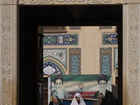 Two veiled Iranian women walk under a banner featuring portraits of Iran's Supreme Leader, Ayatollah Ali Khamenei, and the late leader, Ayat...