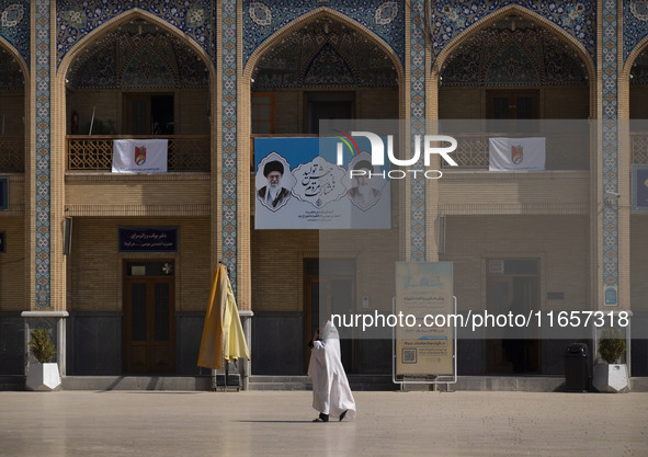 A veiled Iranian woman walks under a banner featuring portraits of Iran's Supreme Leader, Ayatollah Ali Khamenei, and the late leader, Ayato...