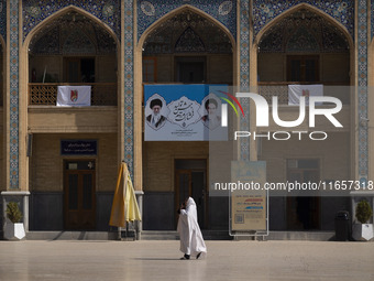 A veiled Iranian woman walks under a banner featuring portraits of Iran's Supreme Leader, Ayatollah Ali Khamenei, and the late leader, Ayato...