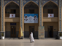 A veiled Iranian woman walks under a banner featuring portraits of Iran's Supreme Leader, Ayatollah Ali Khamenei, and the late leader, Ayato...