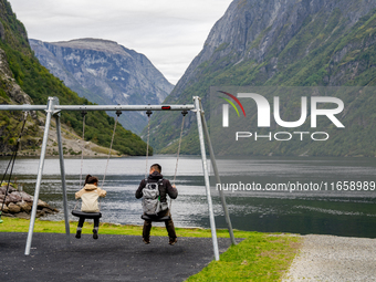 A father and daughter on a swing by the shore in Gudvangen, Norway, on September 17, 2024. The village of Gudvangen is a popular tourist des...