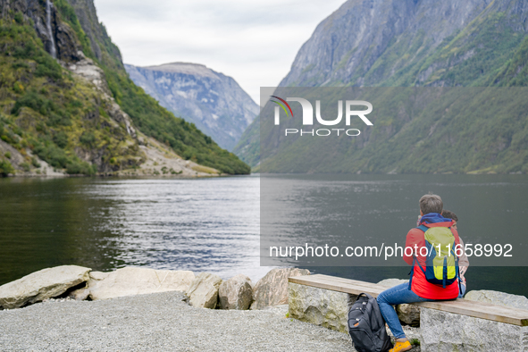 A tourist sits by the water in Gudvangen, Norway, on September 17, 2024. The village of Gudvangen, located at the end of the Nærøyfjord, is...