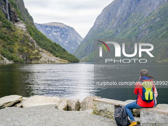 A tourist sits by the water in Gudvangen, Norway, on September 17, 2024. The village of Gudvangen, located at the end of the Nærøyfjord, is...