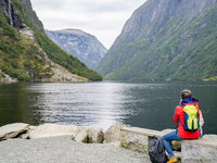 A tourist sits by the water in Gudvangen, Norway, on September 17, 2024. The village of Gudvangen, located at the end of the Nærøyfjord, is...