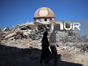 Palestinians walk past a mosque after it is hit in an Israeli strike in Khan Younis, in the southern Gaza Strip, on October 12, 2024, amid t...