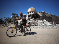 A Palestinian man rides a bicycle beside a mosque after it is bombed in an Israeli airstrike in Khan Younis, southern Gaza Strip, on October...