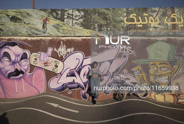 A young Iranian woman poses for a photograph in front of graffiti while standing next to her BMX bike after taking part in a freestyle bicyc...