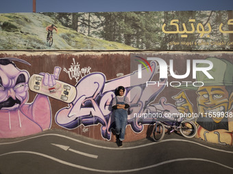 A young Iranian woman poses for a photograph in front of graffiti while standing next to her BMX bike after taking part in a freestyle bicyc...