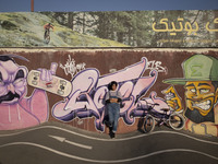 A young Iranian woman poses for a photograph in front of graffiti while standing next to her BMX bike after taking part in a freestyle bicyc...