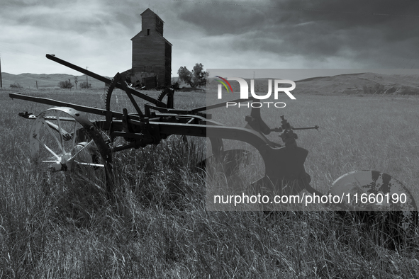 A horse-drawn tiller sits in front of an abandoned grain elevator in the ghost town of Owanka, South Dakota, USA. 