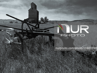 A horse-drawn tiller sits in front of an abandoned grain elevator in the ghost town of Owanka, South Dakota, USA. (