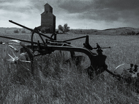 A horse-drawn tiller sits in front of an abandoned grain elevator in the ghost town of Owanka, South Dakota, USA. (