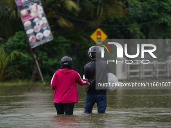 People walk on the flooded road in Kelaniya, Sri Lanka, on October 13, 2024. The adverse weather affects approximately 76,218 people from 18...