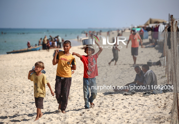 Displaced Palestinian boys walk back to their family's tents at a makeshift camp on the beach of Deir al-Balah, central Gaza Strip, on Octob...